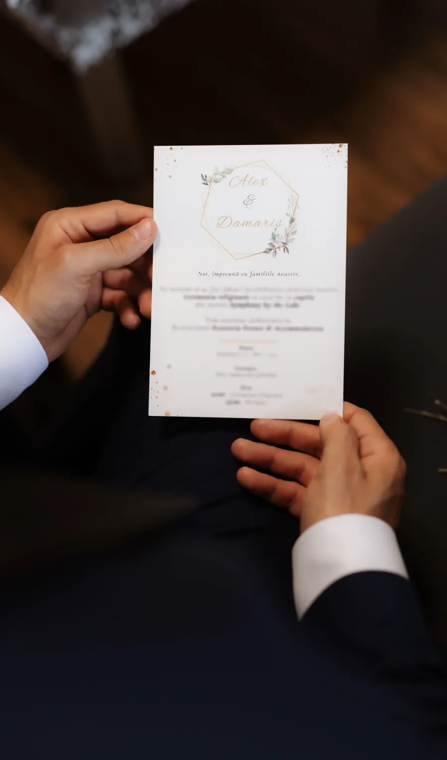 Mirele ține în mâini invitația de nuntă personalizată, cu numele mirilor într-un hexagon auriu cu frunze